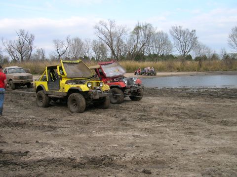 1996 Ford Bronco - Several off-road vehicles are stuck in the mud near a lake, with their hoods open.