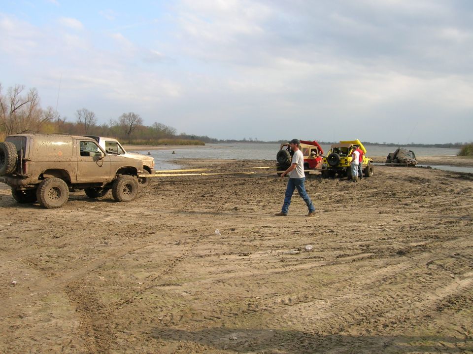 Muddy off-road vehicles being towed on a sandy beach near a lake