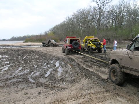 1996 Ford Bronco - Several off-road vehicles are stuck in the mud near a body of water, with one vehicle being towed.