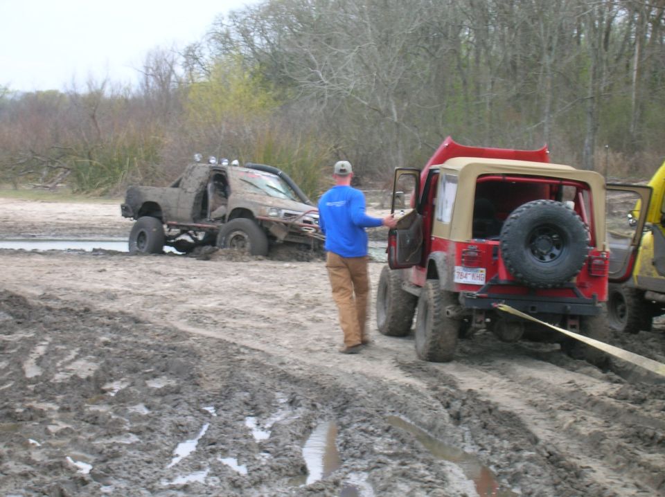 Red Jeep Wrangler rear view, spare tire mounted, being towed out of mud