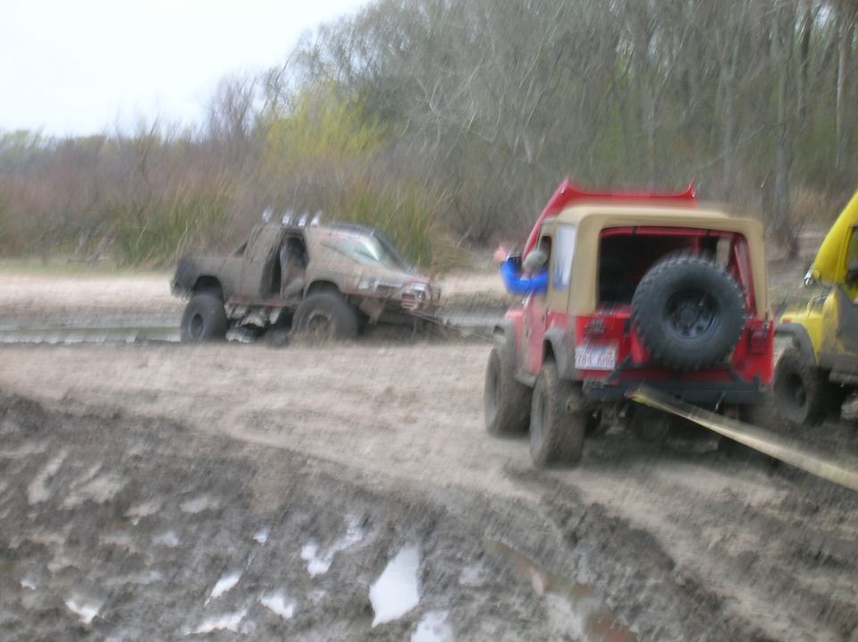 Two off-road vehicles are stuck in thick mud, with one vehicle attempting to pull the other