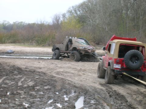 1996 Ford Bronco - Two off-road vehicles are stuck in the mud, with one being towed out by the other.