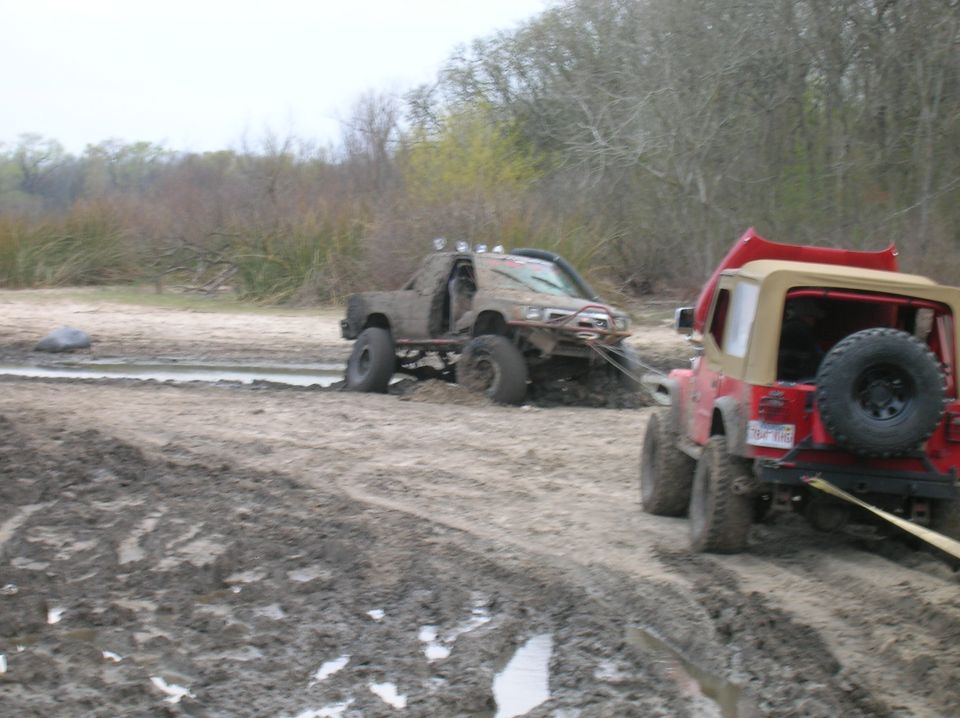 Muddy truck stuck in water, red Jeep pulling it out with a strap