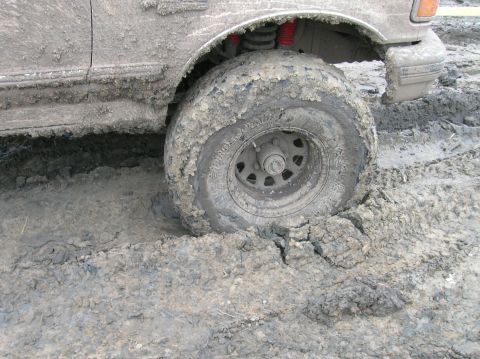 1996 Ford Bronco - A 1996 Ford Bronco is stuck deep in mud, with its tire and fender heavily coated in the thick, wet earth.