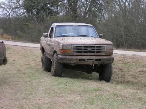 1996 Ford Bronco - Mud-covered pickup truck with lifted suspension and large tires parked on grassy terrain.
