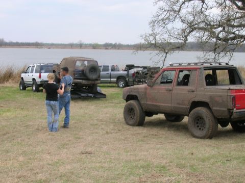 1996 Ford Bronco - A muddy red Jeep Cherokee is parked near a lake with other vehicles and people.
