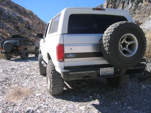 1993 Ford Bronco - Two SUVs drive on a rocky trail in a canyon, with one Ford Bronco in the foreground.