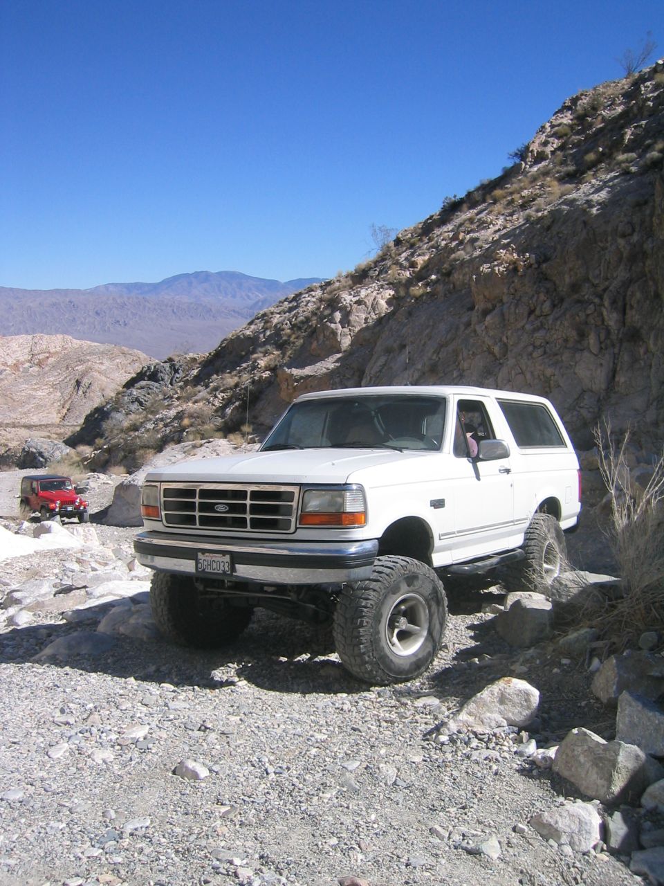White lifted Ford Bronco on big tires parked on rocky desert trail