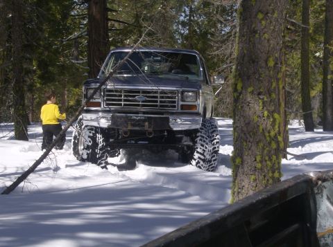 1986 Ford Bronco - A 1986 Ford Bronco navigates through a snowy forest with its large off-road tires.