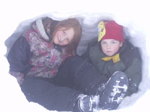 1986 Ford Bronco - Two children sit inside a snow fort, one smiling and the other looking forward.