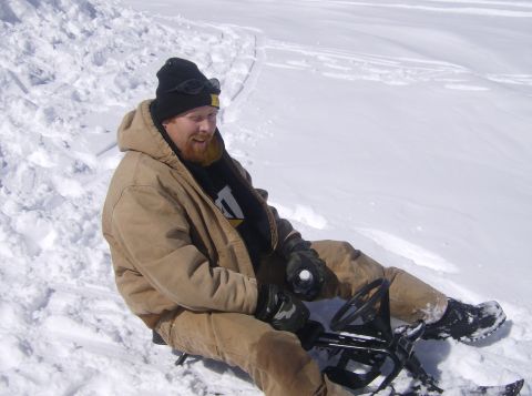 1986 Ford Bronco - Man sits on a snow toy in a snowy area, wearing a beanie and winter jacket.