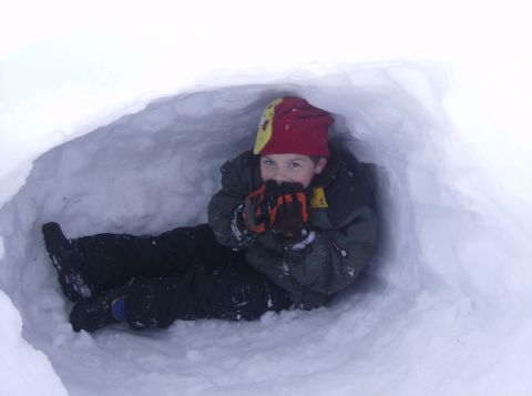 1986 Ford Bronco - A child sits in a snow fort, warming their hands.