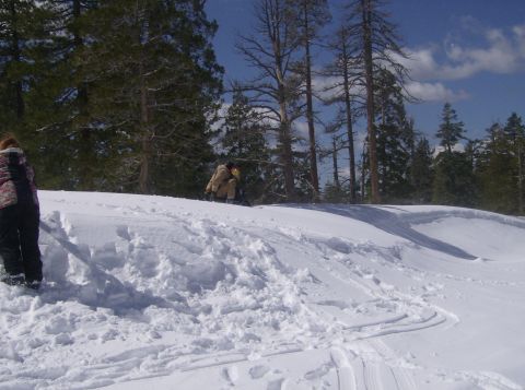 1986 Ford Bronco - A winter scene with two people in the snow, surrounded by trees under a blue sky.