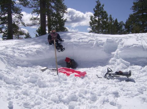 1986 Ford Bronco - Two children enjoy a snowy day, digging into a snow fort with a sled and a snowmobile nearby.