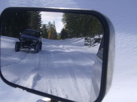 1986 Ford Bronco - A four-wheel-drive vehicle navigates a snow-covered path through a wooded area.