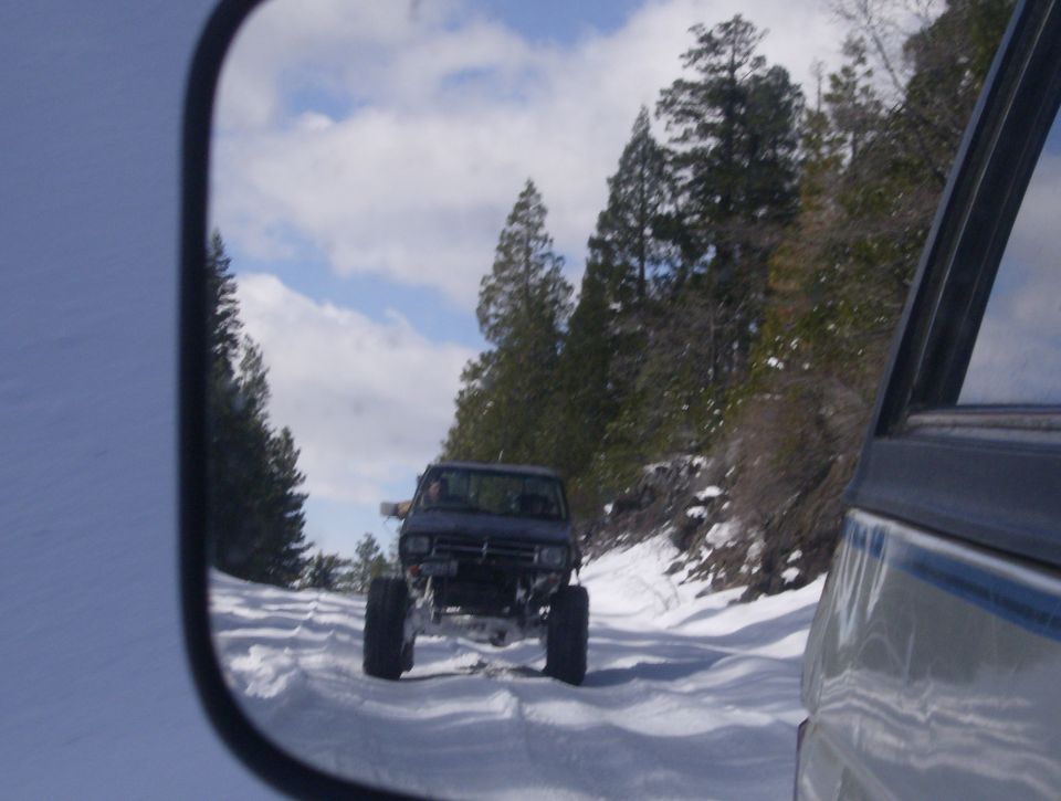 Dark SUV with lifted suspension driving on a snowy road, seen in a side mirror