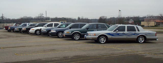 Line of cars including a flamed Lincoln Town Car in a parking lot