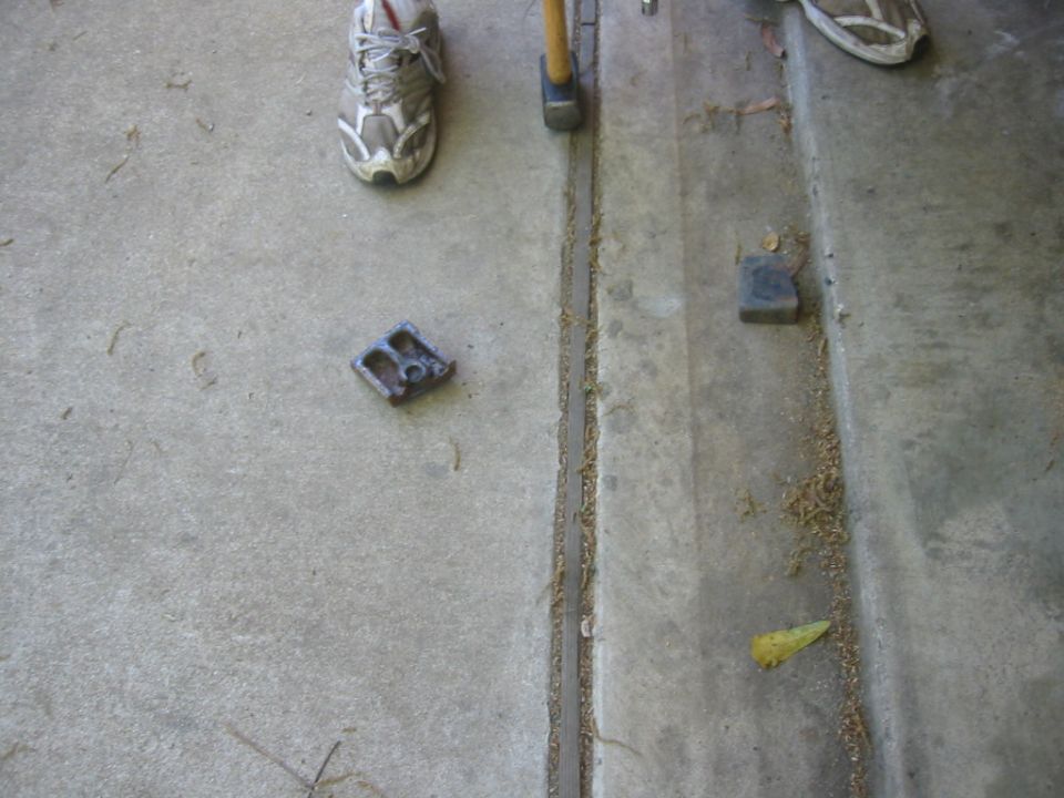 metal bracket on concrete floor next to a hammer and shoes