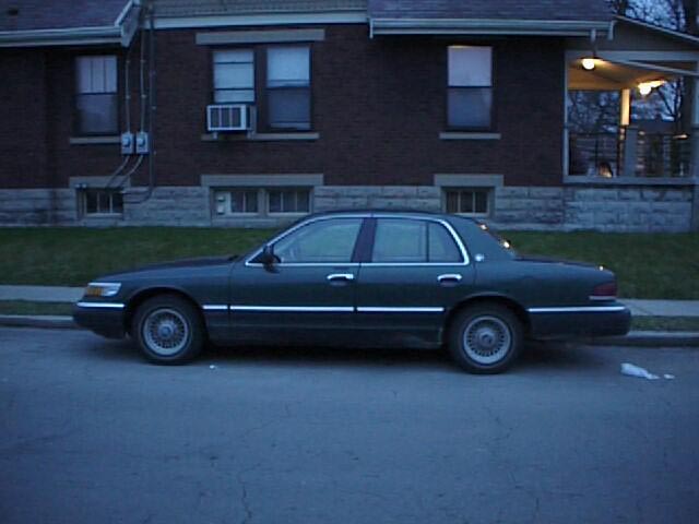 Dark green Mercury Grand Marquis sedan parked on street by brick house