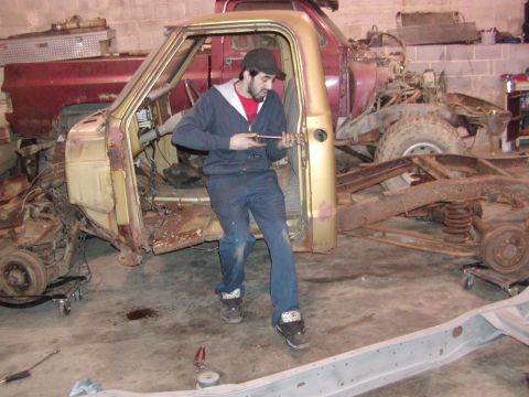1991 Ford Bronco - Disassembled truck frame with a man working on it; another truck is in the background.