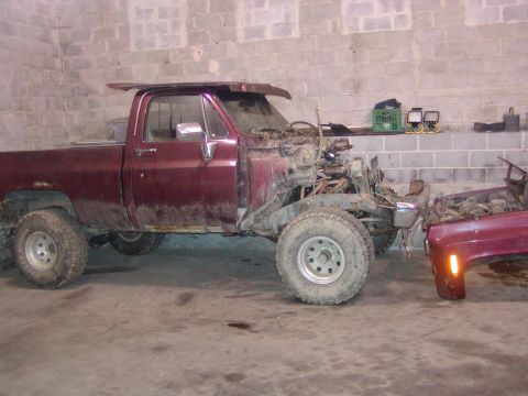 1991 Ford Bronco - A maroon pickup truck, likely from the 1980s, sits in a garage with its engine compartment exposed and a separate fender nearby.