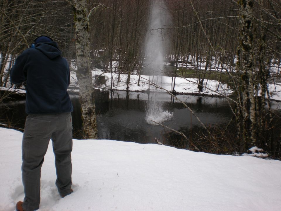 Person standing in snow near a river with water spraying up