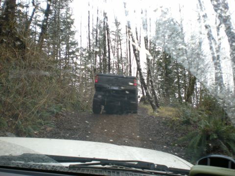 1993 Ford Bronco - A black SUV navigates a wet, wooded path, viewed from the perspective of a following vehicle.
