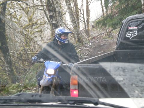 1993 Ford Bronco - A dirt biker rides through a wooded trail next to a Toyota pickup truck.