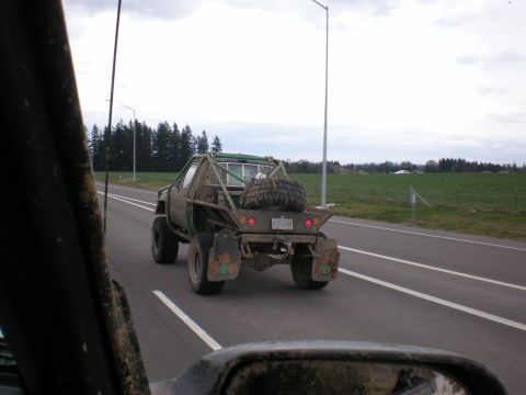 1993 Ford Bronco - A heavily modified pickup truck with a flatbed and roll cage is seen driving on a highway.