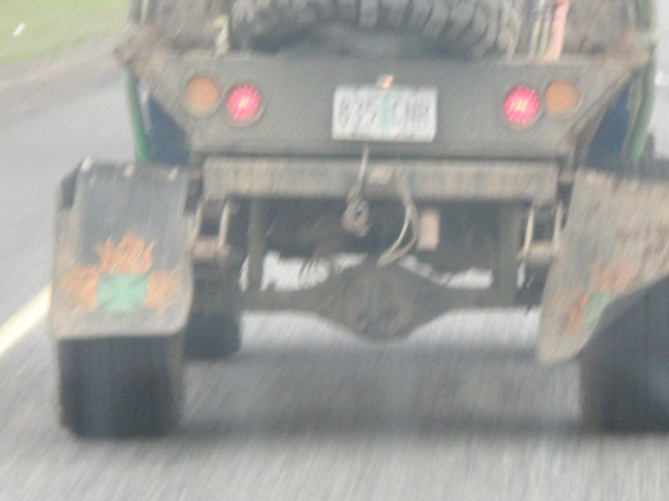 Mud-splattered truck rear with dual rear wheels and a spare tire mounted above. The license plate is visible