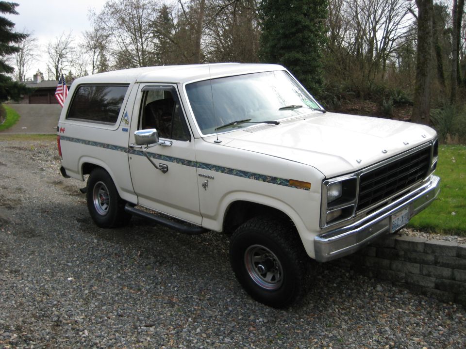 White 1980 Ford Bronco parked on gravel, front 3/4 view. Decorative stripe on side