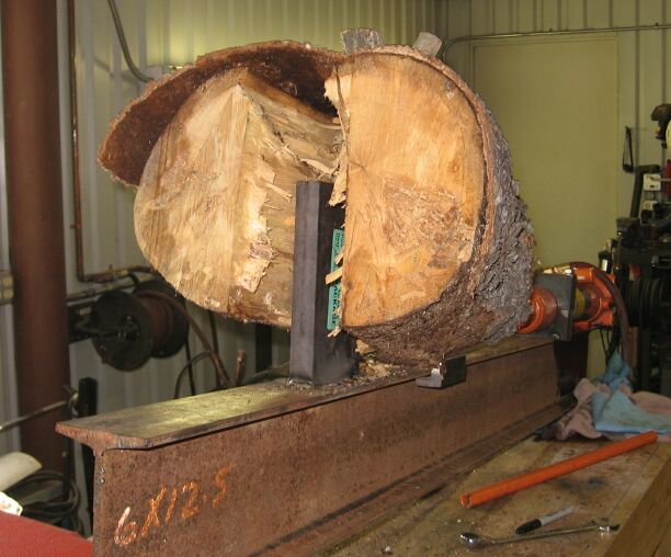 Split log clamped on a steel beam log splitter in a workshop
