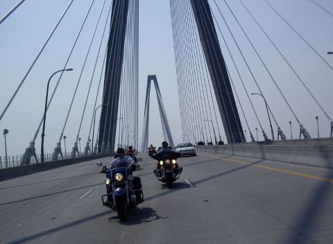 2005 BMW R1200CA ABS - Motorcycles ride on a bridge with tall towers and cables overhead.