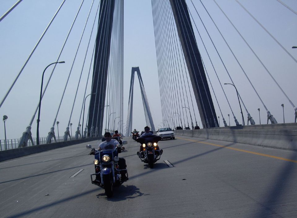 Several motorcycles and a car drive across a large cable-stayed bridge