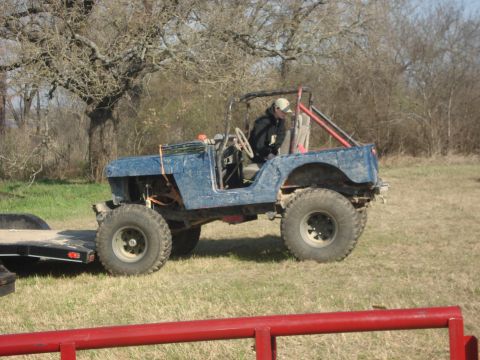 1989 Ford Bronco II - Modified Jeep with roll cage and large tires is parked next to a trailer in a grassy field.