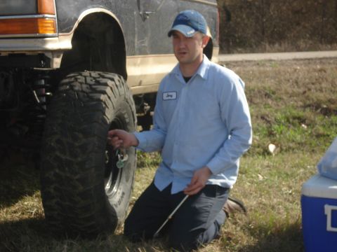 1989 Ford Bronco II - A man kneels beside a 1989 Ford Bronco II, checking the tire pressure on its large off-road tire.