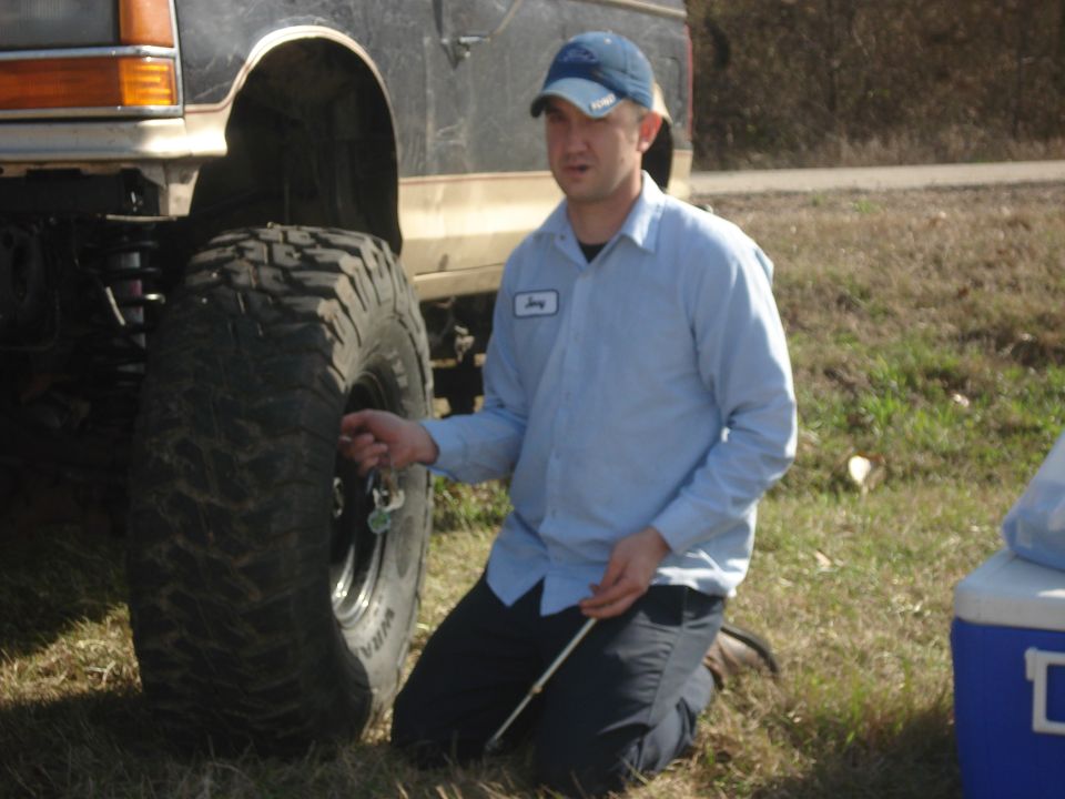 Side view of a 1989 Ford Bronco II with large off-road tires, a man checks tire pressure