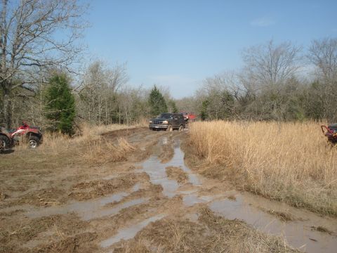 1989 Ford Bronco II - Off-road vehicles navigate a challenging muddy track under a clear blue sky.