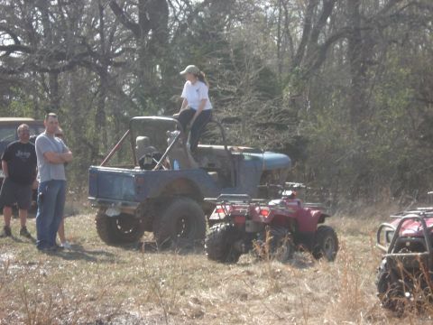 1989 Ford Bronco II - Several off-road vehicles, including ATVs and a modified Jeep, are parked in a grassy, wooded area with people standing around.