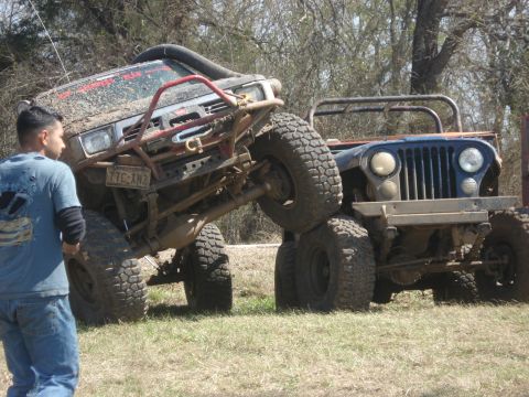 1989 Ford Bronco II - Two heavily modified off-road vehicles are stuck in a grassy area, one atop the other.