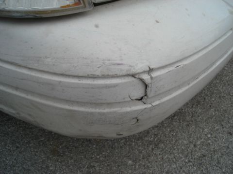 2000 Ford Crown Victoria - Close-up of a damaged white car bumper with visible cracks and wear.
