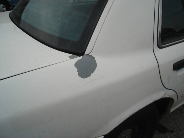 White sedan rear quarter panel with gray primer showing through chipped paint
