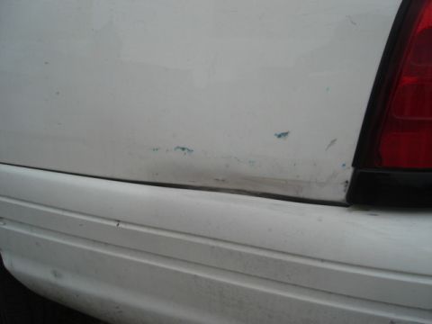2000 Ford Crown Victoria - The rear of a white vehicle shows damage to the quarter panel, including a dent and paint transfer.