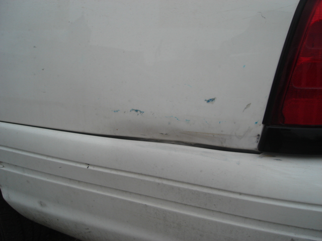White car's rear quarter panel has a dent and some scuffs near the taillight