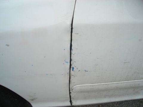 2000 Ford Crown Victoria - Close-up of a white car's door seam shows damage and wear.