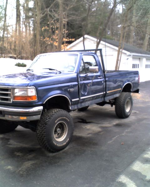 1996 Ford F-150 - A blue 1996 Ford F-150 pickup truck is parked in a driveway with a house and trees in the background.