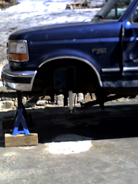 1996 Ford F-150 - Front quarter panel and suspension of a blue 1996 Ford F-150 truck, elevated on jack stands for maintenance.