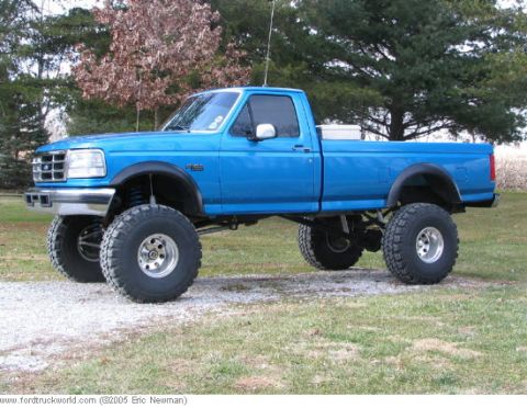 1996 Ford F-150 - This lifted pickup truck has oversized tires and is parked on a gravel surface with trees in the background.