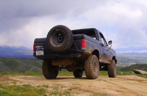 1990 Ford Bronco - A black 1990 Ford Bronco is parked on a hill overlooking a valley under a cloudy sky.
