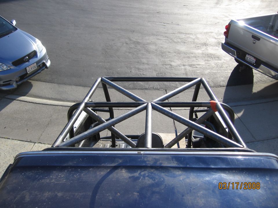 Pickup truck bed with a metal roll cage, silver car to the left, silver pickup truck to the right